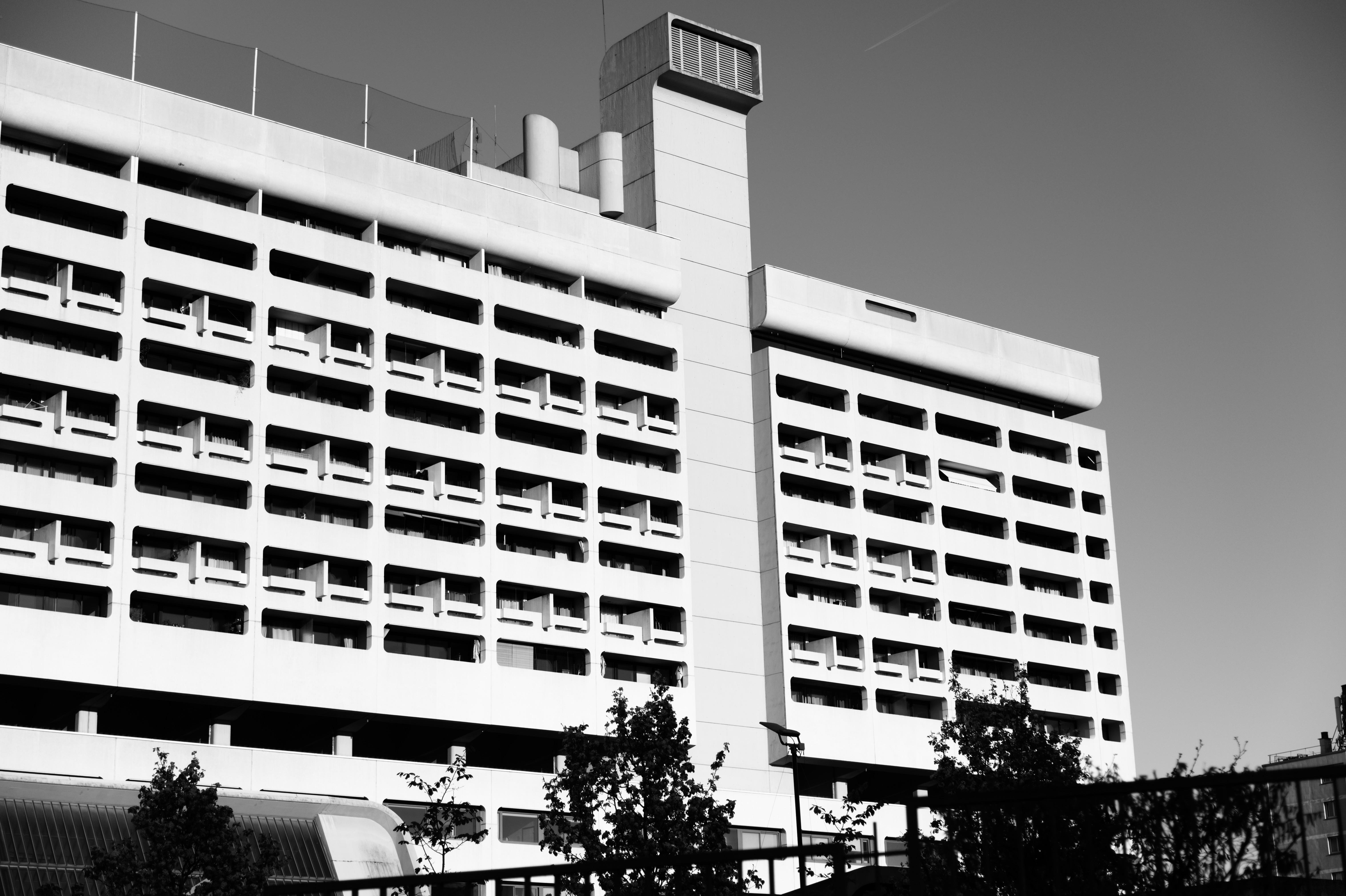 Modernist high-rise with rooftop structures and silhouetted trees